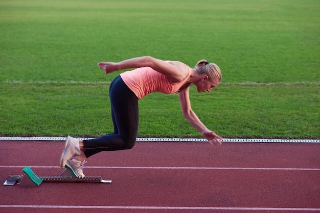 woman  sprinter leaving starting blocks on the athletic  track. Side view. exploding start