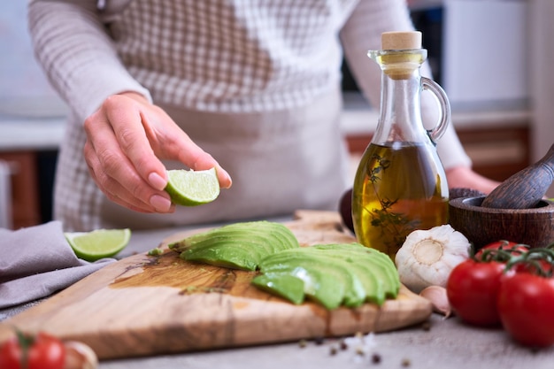 Woman squeeze fresh lime juice onto Sliced avocado on wooden cutting board at domestic kitchen