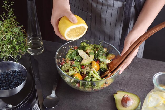 Photo woman squeezing lemon into delicious superfood salad in kitchen