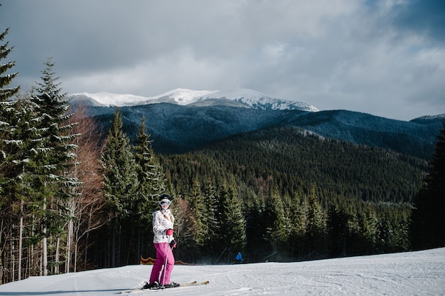 Woman stand skiing, is preparing descend down on snow track in Carpathian mountains. On background forest and ski slopes.