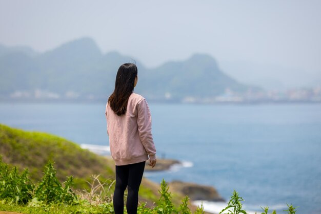 崖の頂上に立って海を見ている女性