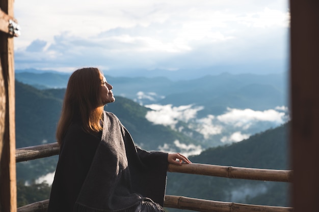 朝の青い空と霧の日に山を見てバルコニーに一人で立っている女性