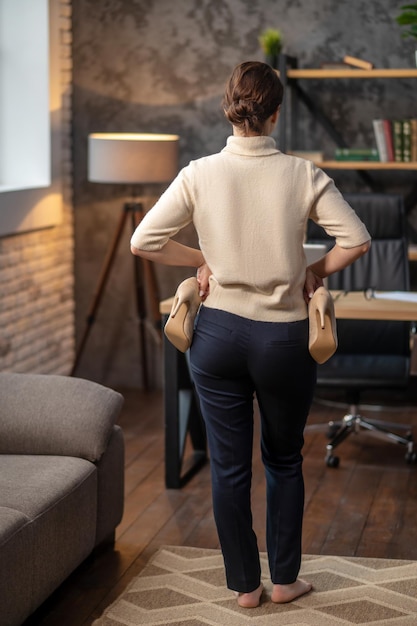 A woman standing backside with beige shoes in hands