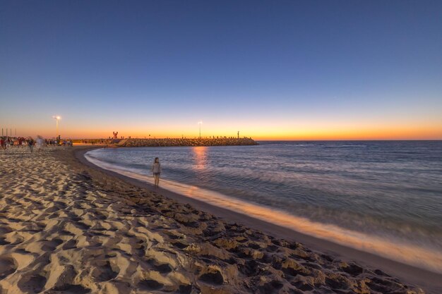 Woman standing at beach against clear blue sky at dusk