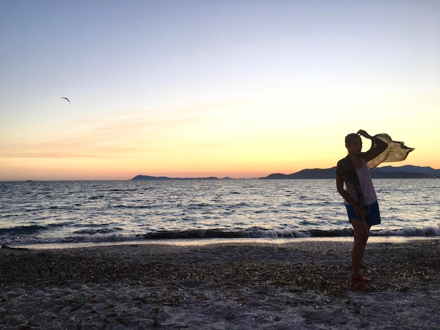 Photo woman standing on beach against sky during sunset