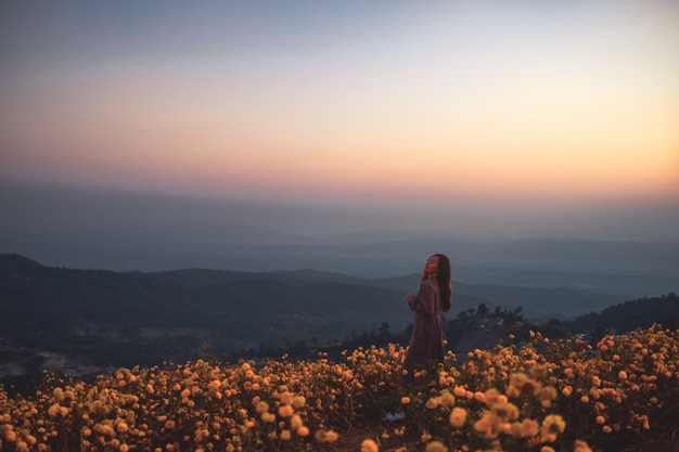 일출 전에 언덕 꼭대기에 아름다운 꽃밭 사이에 서 있는 여자