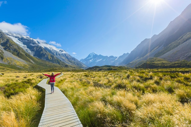 Woman standing on boardwalk by plants and mountains against sky