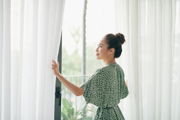 居間の窓とカーテンを開けて立っている女性