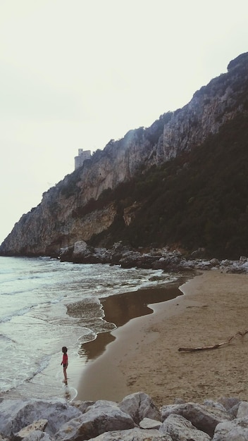 Foto donna in piedi su una scogliera vicino al mare contro un cielo limpido