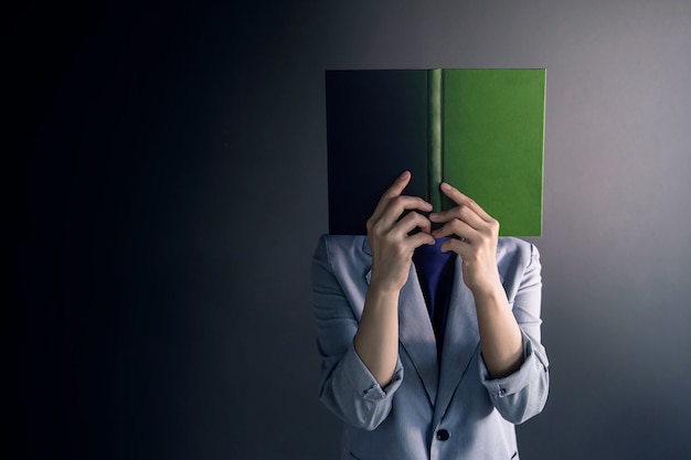 Woman Standing at Dark wall and Face covered by Book