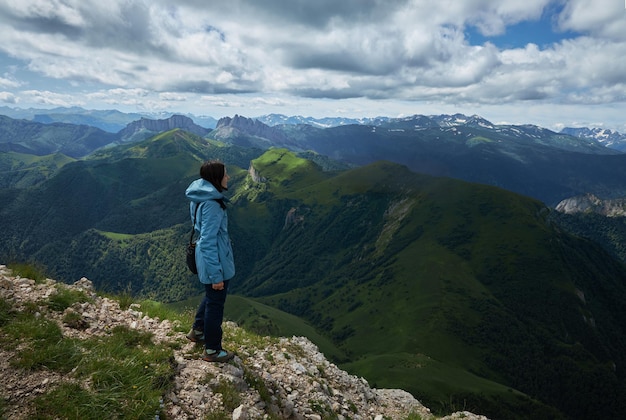 Woman standing at the edge of a cliff overlooking high mountains woman looking out over an idyllic mountain scene