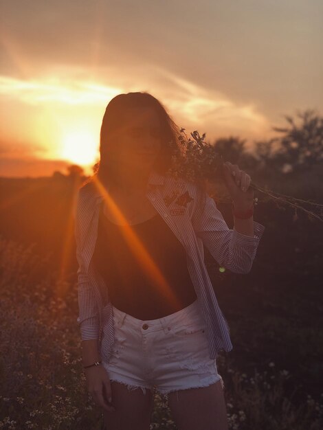 Woman standing on field against sky during sunset