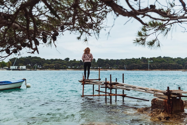 Woman standing on fishing pier looking at not calm sea