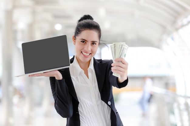 Woman standing holding working with a laptop and money 