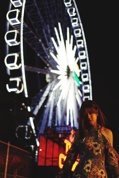Photo woman standing at illuminated ferris wheel