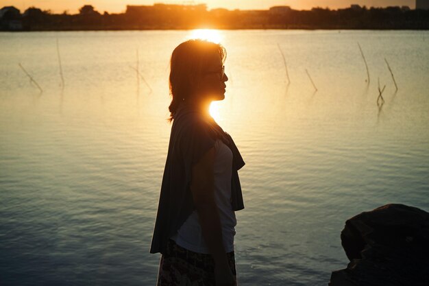 写真 夕暮れの空に向かって湖に立っている女性