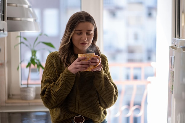 Woman standing in the kitchen and drinking cup of tea