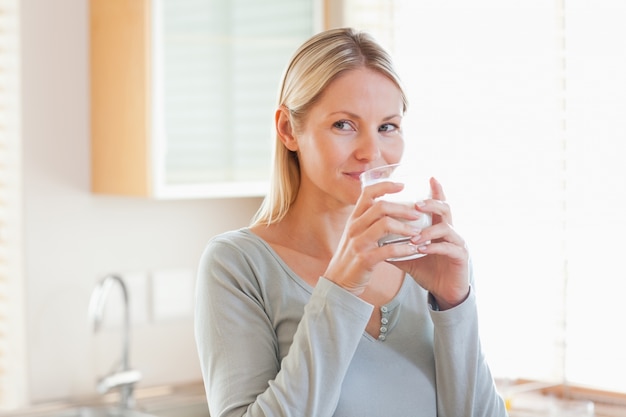 Photo woman standing in the kitchen drinking some water