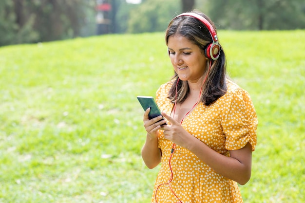 Woman standing listening to music with headphones while texting with her mobile phone