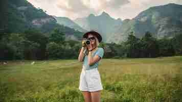 Photo woman standing on meadow and holding camera take photo at phu chi fa mountains in chiangrai thaila