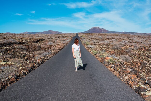 Woman standing in the middle of a deserted road on a sunny day.