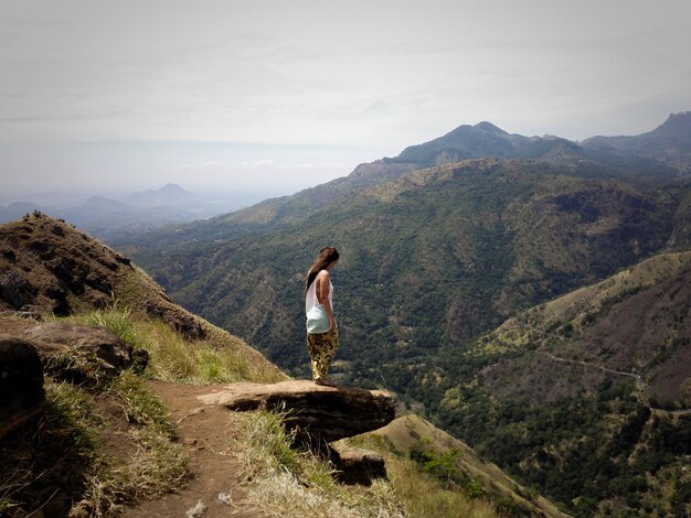 Woman standing at mountain against cloudy sky