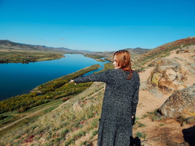 Женщина стоит на горе у озера напротив неба