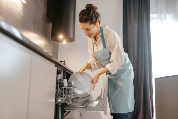 Woman standing near the dishwasher and taking plates out