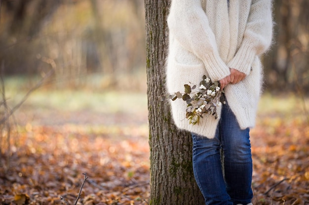 Woman standing near the tree and holding seasonal bouquet in her hands on a sunny day in the park