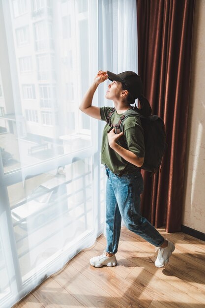 Woman standing near window at home with backpack