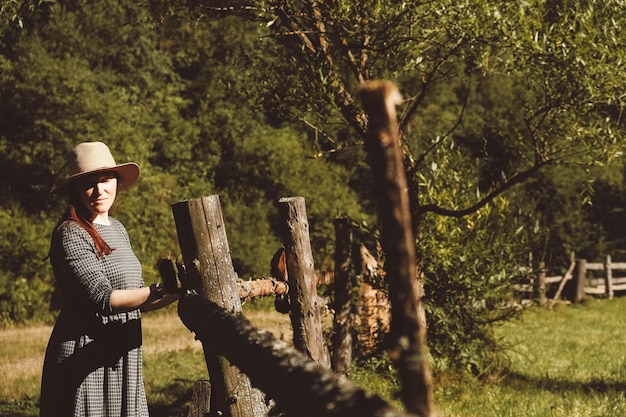 Woman standing near a wooden fence on a background of forest and trees at sunset