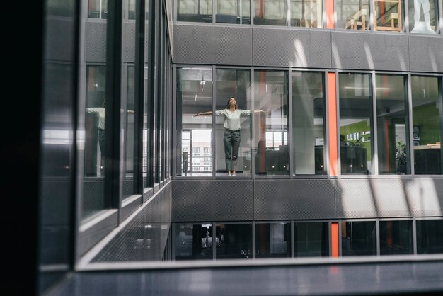 Woman standing at office window, with arms outstretched