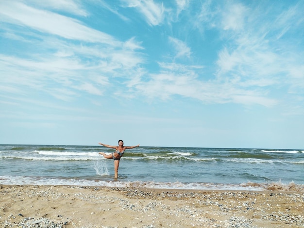 Woman standing on one leg at beach against sky