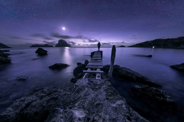 Foto donna in piedi sul molo sopra il mare di notte