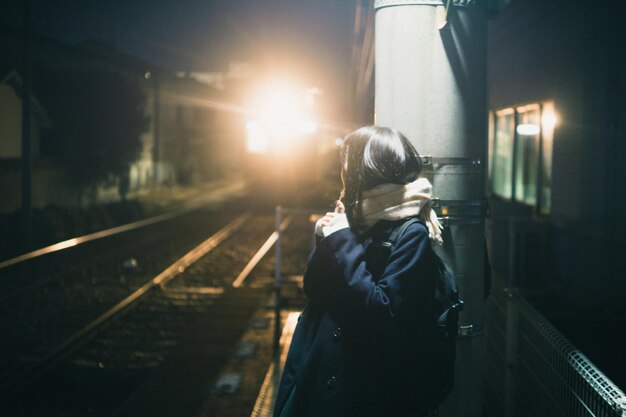 Photo woman standing on railroad station platform at night