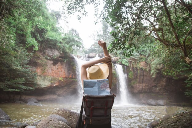 A woman standing in the river with her Raised hands to waterfall.