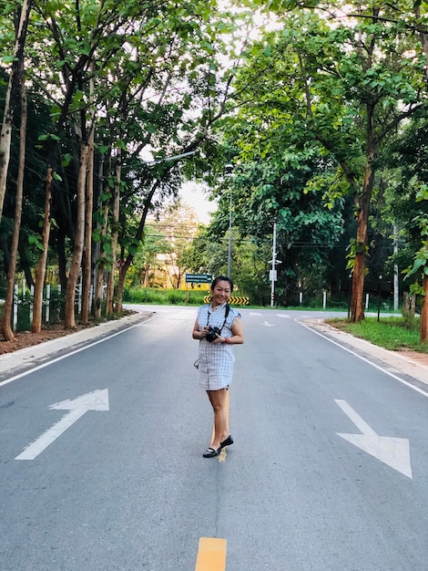 Foto donna in piedi sulla strada in mezzo agli alberi