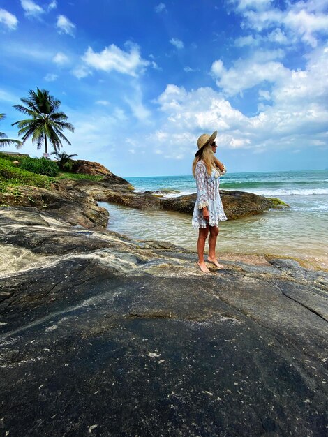 Woman standing on rock at beach against sky