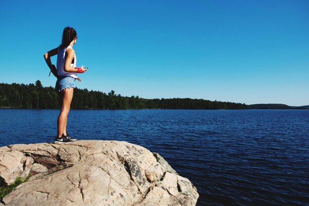 Woman standing on rock by lake against sky