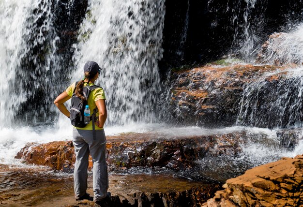 Woman standing on a rock looking at a waterfall ecotourism concept