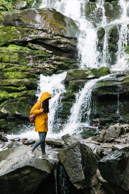 Woman standing on rock in yellow raincoat with waterfall on background