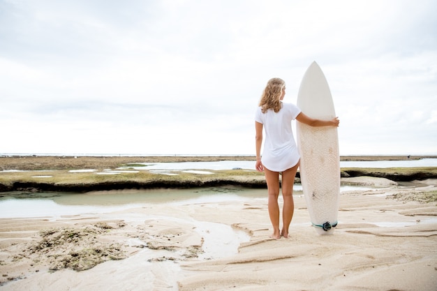 Foto donna in piedi sulla spiaggia di sabbia con surfboard