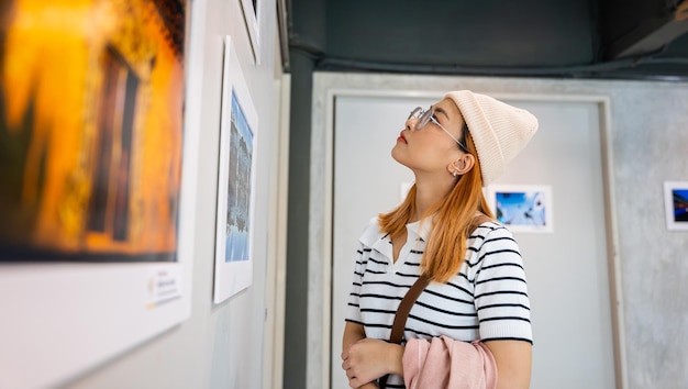 Woman standing she looking art gallery collection in front framed paintings pictures