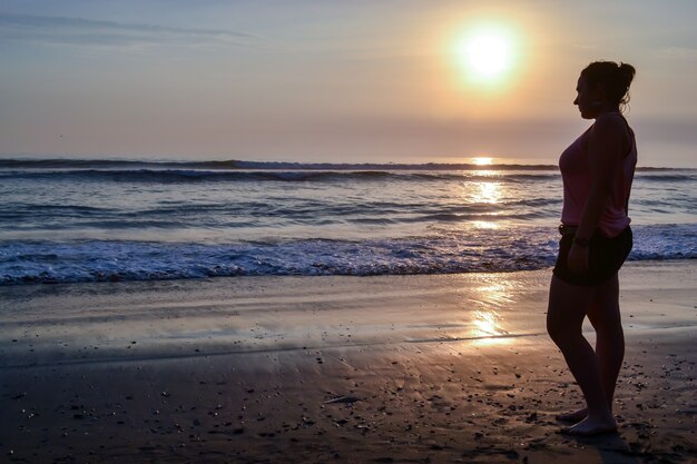 Donna in piedi sulla riva di una spiaggia al tramonto