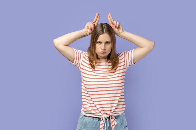 Woman standing and showing horns being anger and aggressive looking at camera