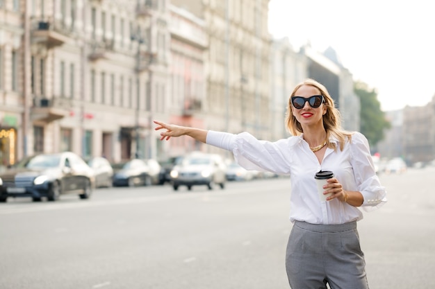 Woman standing on the street with coffee and catches a car