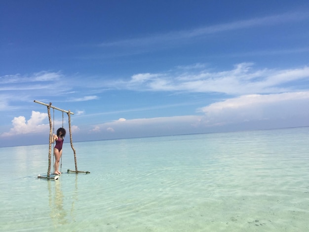 Photo woman standing on swing over sea against sky