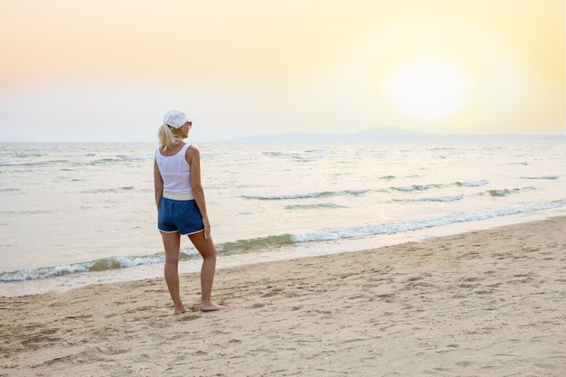 夕暮れ時にビーチに立って太陽を見ている女性