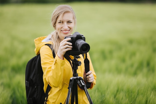 Женщина, стоящая на пшеничном поле со штативом и камерой