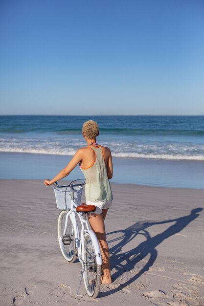 Photo woman standing with bicycle on beach in the sunshine